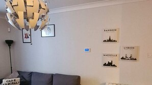 Ein modernes Wohnzimmer mit einem grauen Ecksofa, einer ungewöhnlichen, kugelförmigen Chandelüster und Wandbildern zum Thema Stadt.