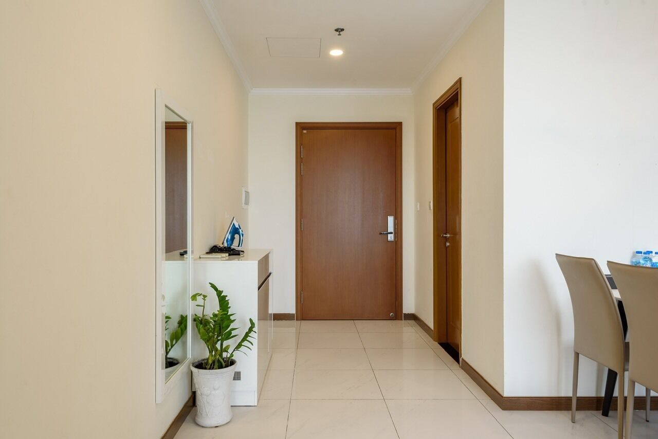 A hallway with a wooden door, a white reception desk, a potted plant, and a dining area with chairs.