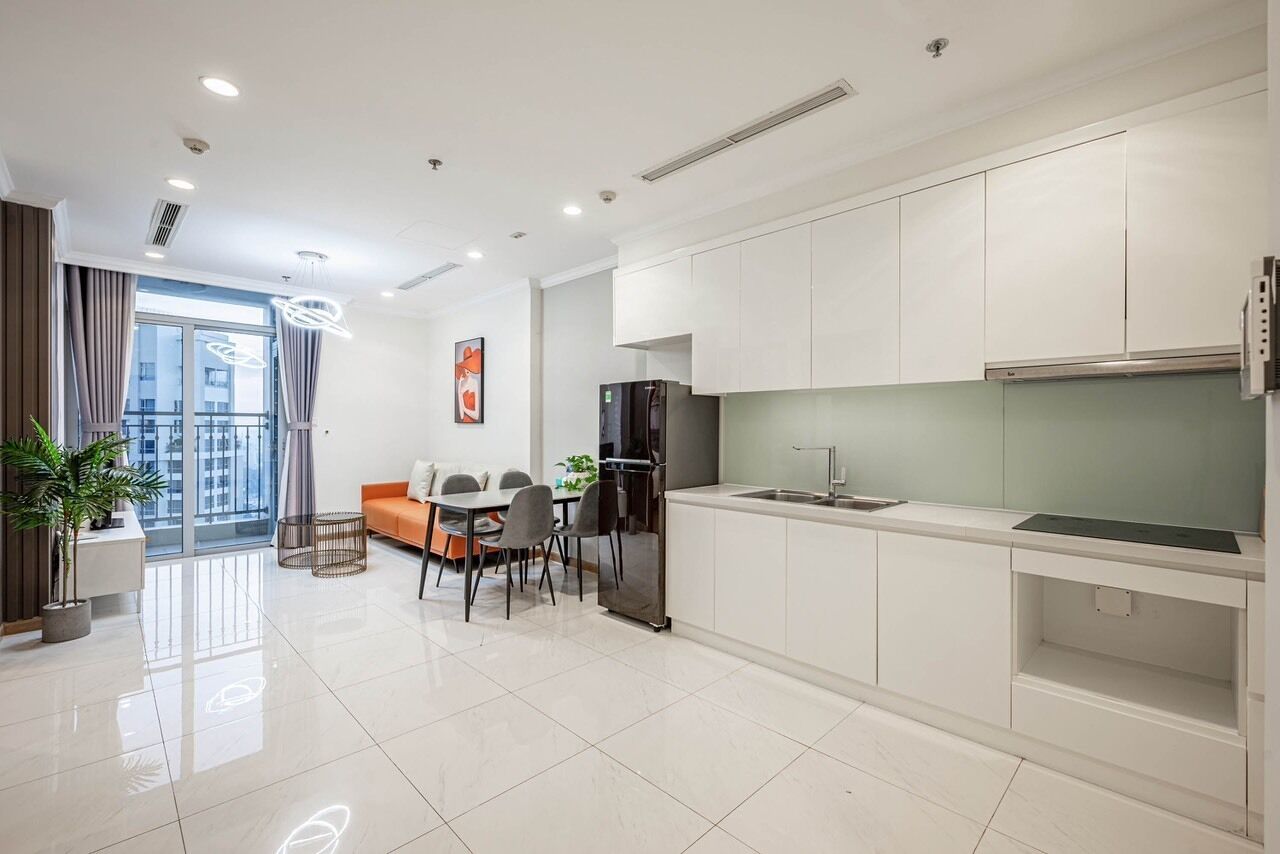 Una cocina moderna con armarios blancos, un comedor con mesa y sillas, y un ventanal con cortinas.