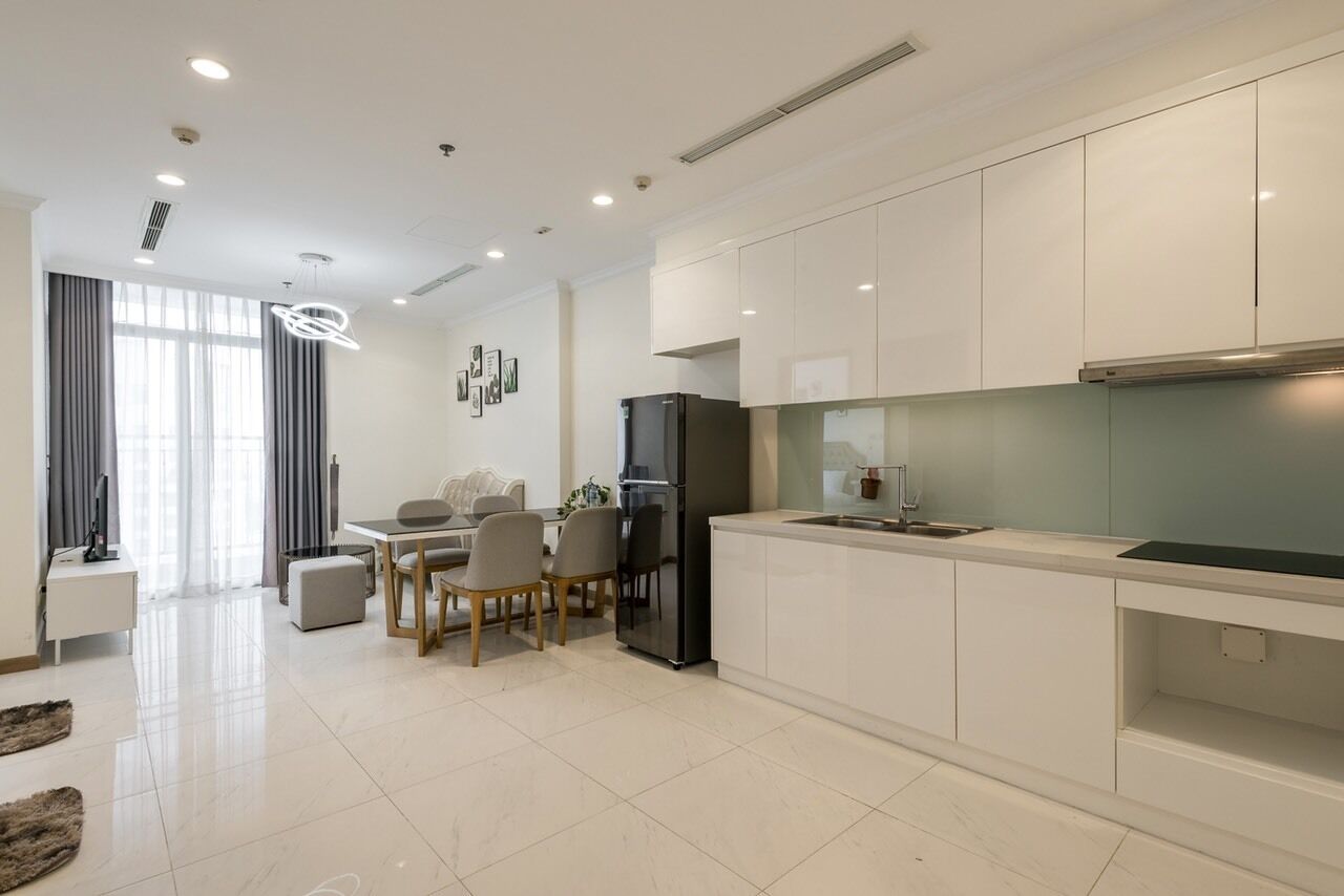 Una cocina moderna con armarios blancos, un refrigerador negro y un comedor con mesa y sillas.