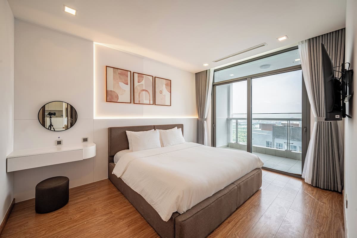 Ein modernes Schlafzimmer mit einem großen Bett, einem Nachttisch, einem Spiegel und Blick auf die Stadt durch ein großes Fenster.