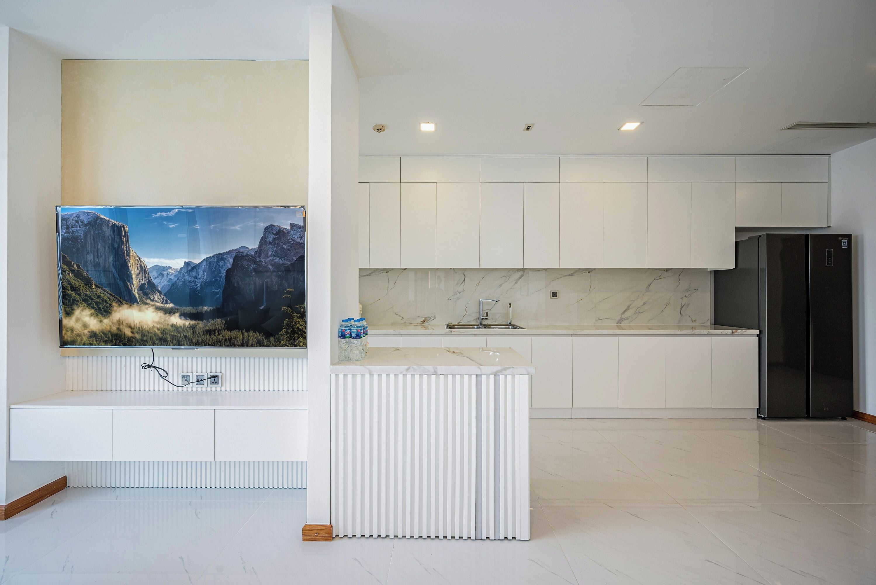 A modern kitchen with white cabinetry, a marble countertop, and a black refrigerator.