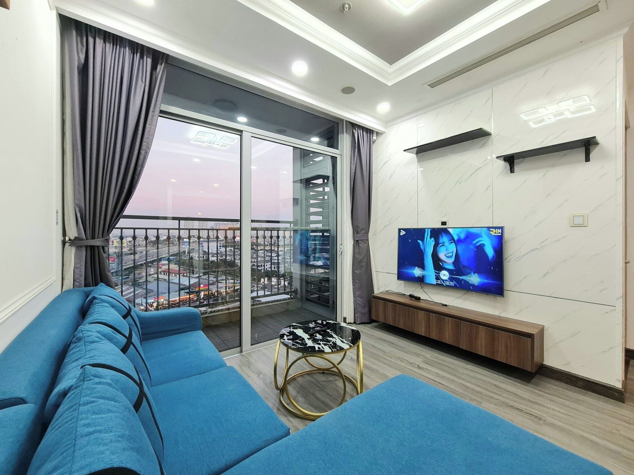 A modern living room with a sofa, a TV, and a balcony with a city view.