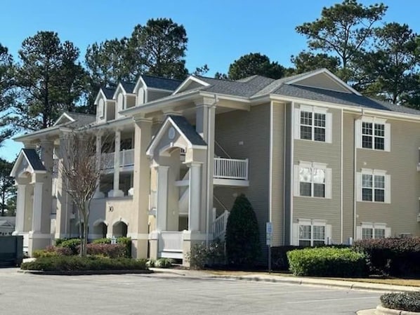 A multi-story building with a symmetrical facade, balconies, and a parking lot in front. - Beaches and Birdies II - First Floor Golf Resort Studio (Calabash)