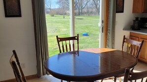 Un comedor con una mesa redonda y cuatro sillas de madera. Hay un ventanal corredero que da a un área exterior con césped.