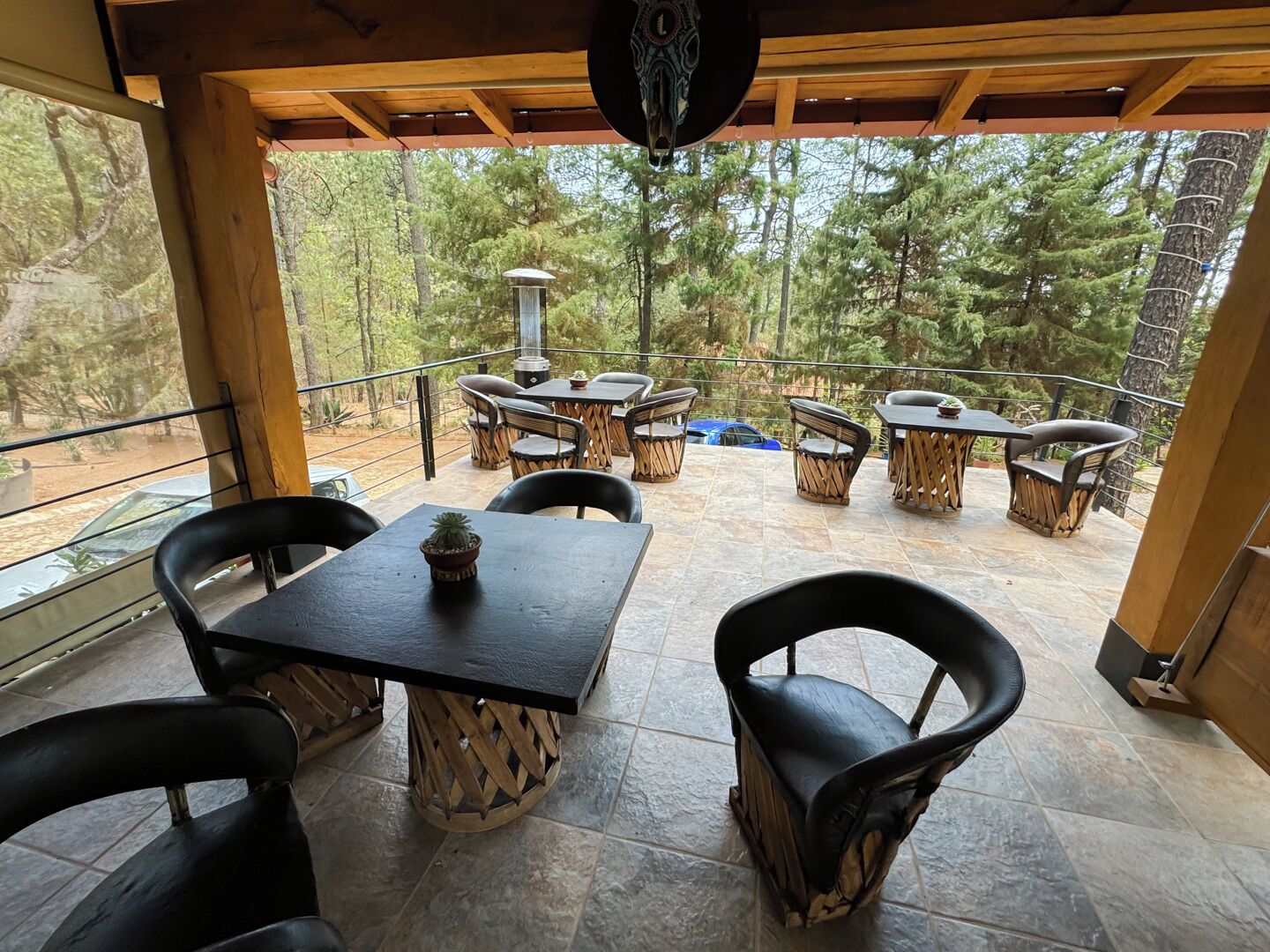 Eine Terrasse im Freien mit Steinböden, Holzmöbeln und Blick auf einen bewaldeten Bereich.