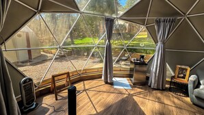 A geodesic dome room with a wooden floor, a small table with a coffee maker, and a view of a garden through large windows. - Luahara Glamping Tapalpa – Domo Natural Experience (Tapalpa)