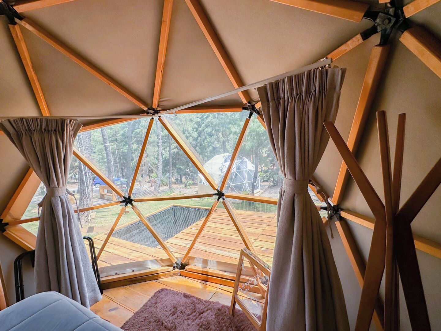Une pièce en forme de dôme géodésique offrant une vue sur une terrasse en bois et des arbres.