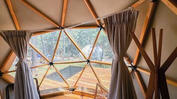 Une pièce en forme de dôme géodésique offrant une vue sur une terrasse en bois et des arbres.