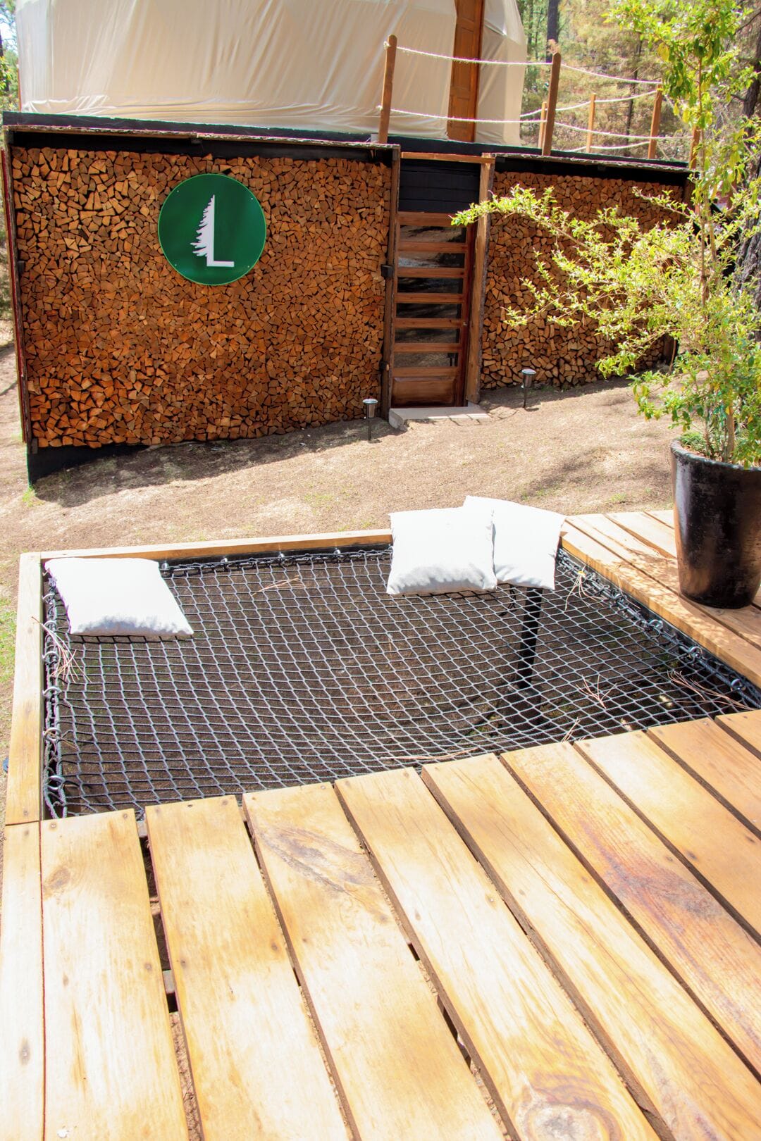 Een houten terras met een zwembad van metalen gaas, een houten deur en een stapel hout voor de kachel.