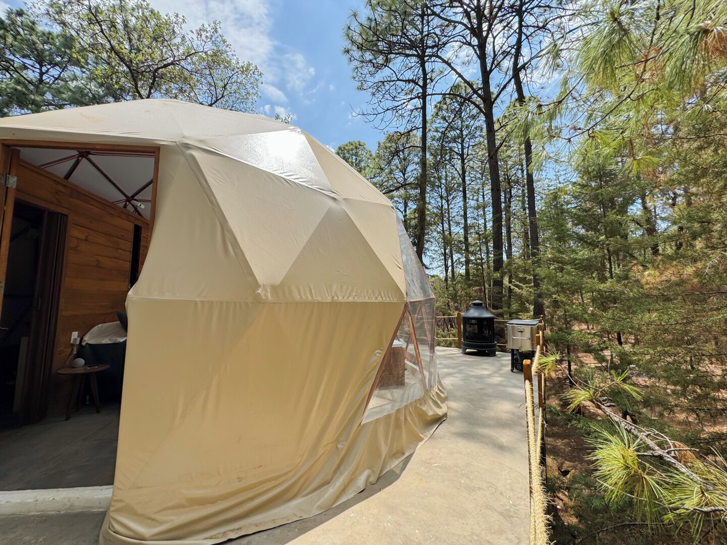 A geodesic dome tent with a door open, revealing a wooden interior with a table and chairs.