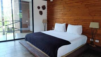 A bedroom with a large bed, wooden panel walls, a glass door leading to an outdoor area, and a nightstand with a lamp.
