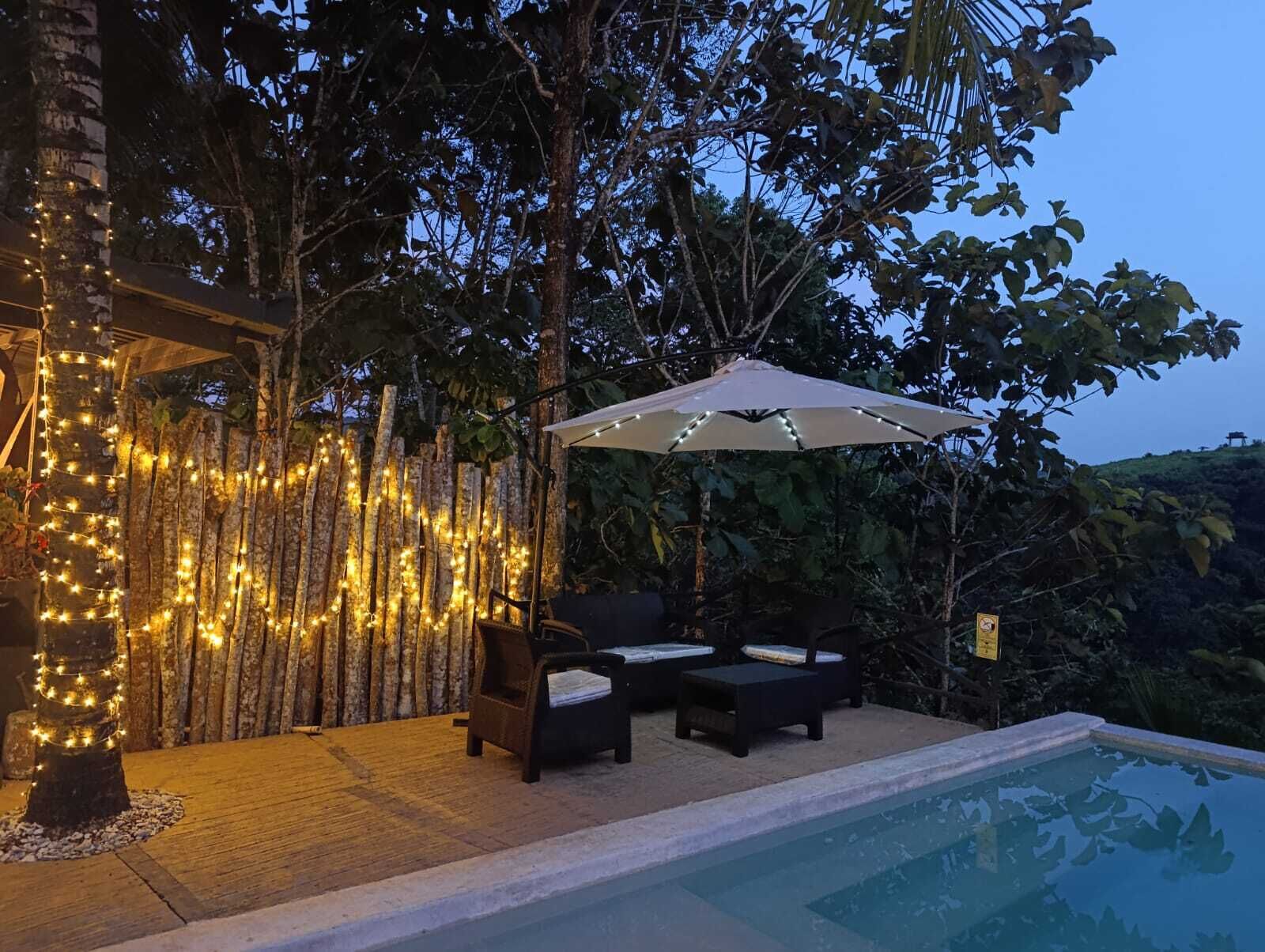 An outdoor seating area with a pool, surrounded by trees and string lights.