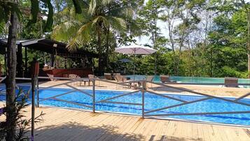 A pool area with a wooden deck, lounge chairs, and umbrellas.