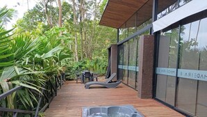 Une terrasse en bois avec un jacuzzi, des sièges d’extérieur et une végétation luxuriante.