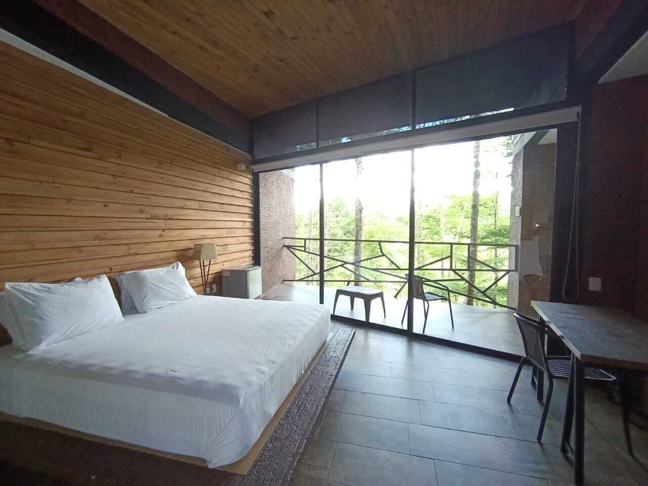 A bedroom with a large bed, a dining table, and a balcony with chairs.