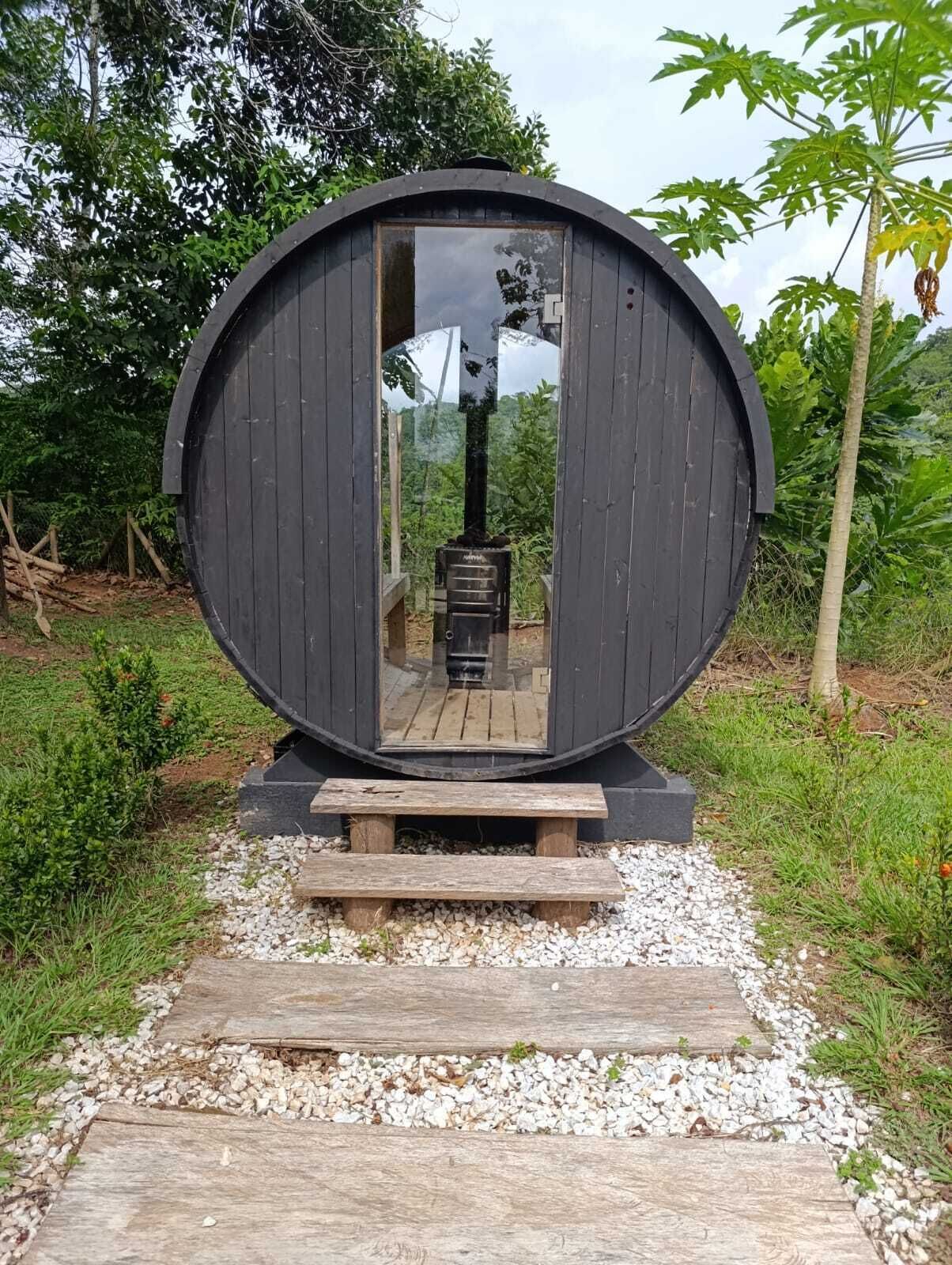 Een ronde houten constructie met een reflecterend oppervlak, een houten bank ervoor en een grindpad er naartoe.