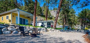 A yellow cabin with a covered porch, surrounded by large rocks and pine trees. - Cozy Cottage by the Lakeshore #4 (West Kelowna)