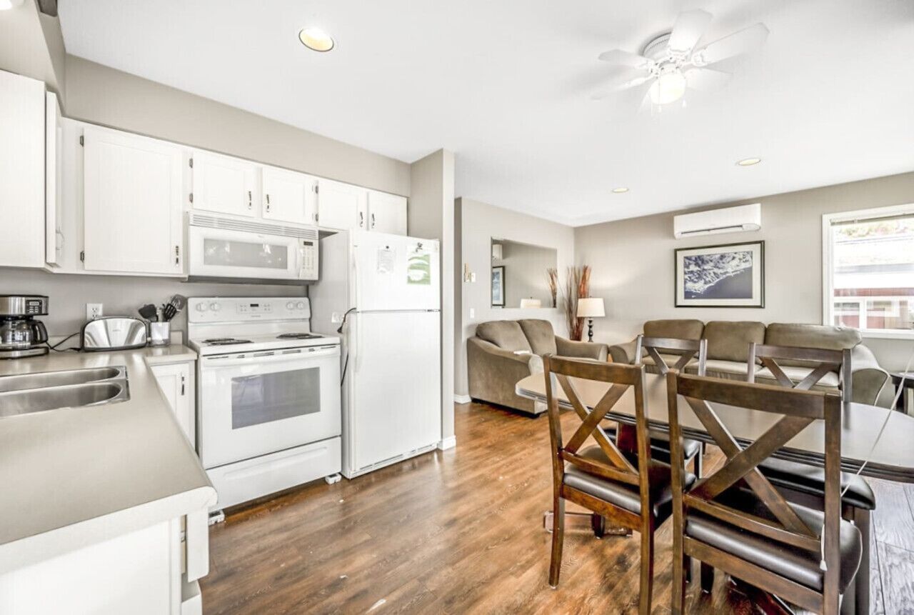 A modern kitchen with white cabinets, a microwave, stove, and refrigerator. There is a dining area with a table and chairs.
