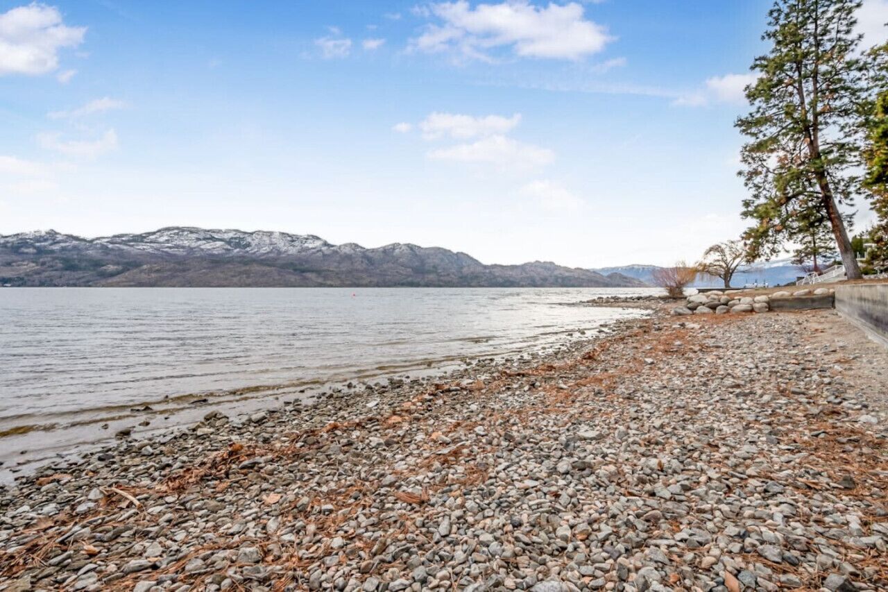 Uma praia de pedras com vista para montanhas distantes e um lago calmo.