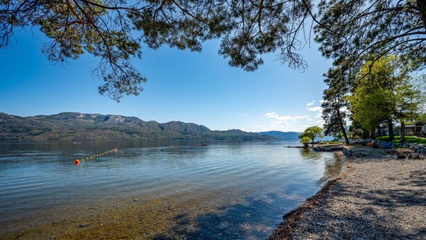 Vista d'un llac amb aigua cristal·lina, una platja de pedres i muntanyes a la distància.