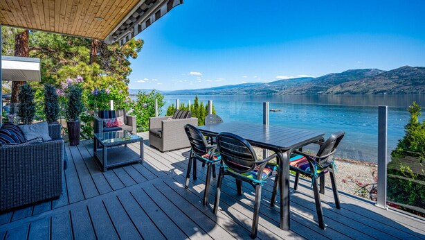 A wooden deck with outdoor furniture, a view of a lake, and surrounding greenery. - Lakeside Serenity Retreat #10 (West Kelowna)