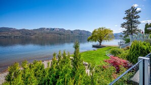 A lakeside view with a clear sky, a grassy area, and a tree. - Lakeside Serenity Retreat #10 (West Kelowna)