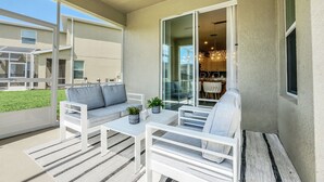 A balcony with a white sofa, a small table, and a chair. There is a glass door leading to an indoor area with a chandelier. - Ultimate Bespoke 6 Bedroom Champions Gate Pool Villa (Davenport)