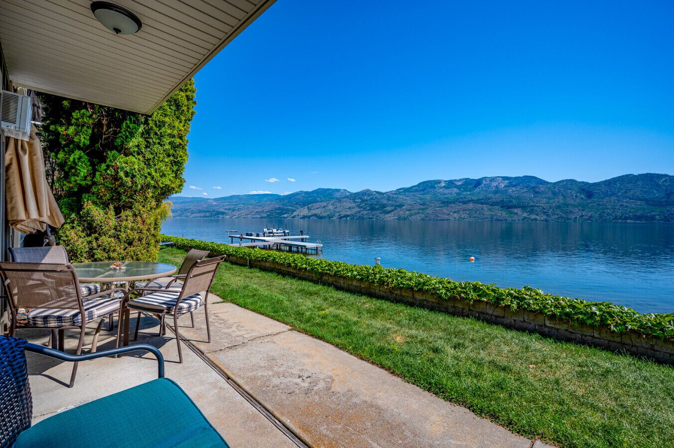 A patio with outdoor furniture overlooking a lake, a dock, and distant mountains.
