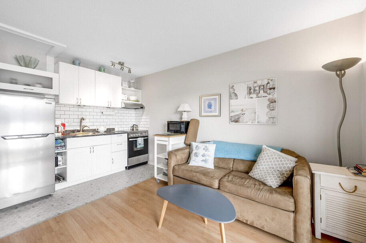 A compact living space with a kitchenette, a sofa, a coffee table, and a lamp.