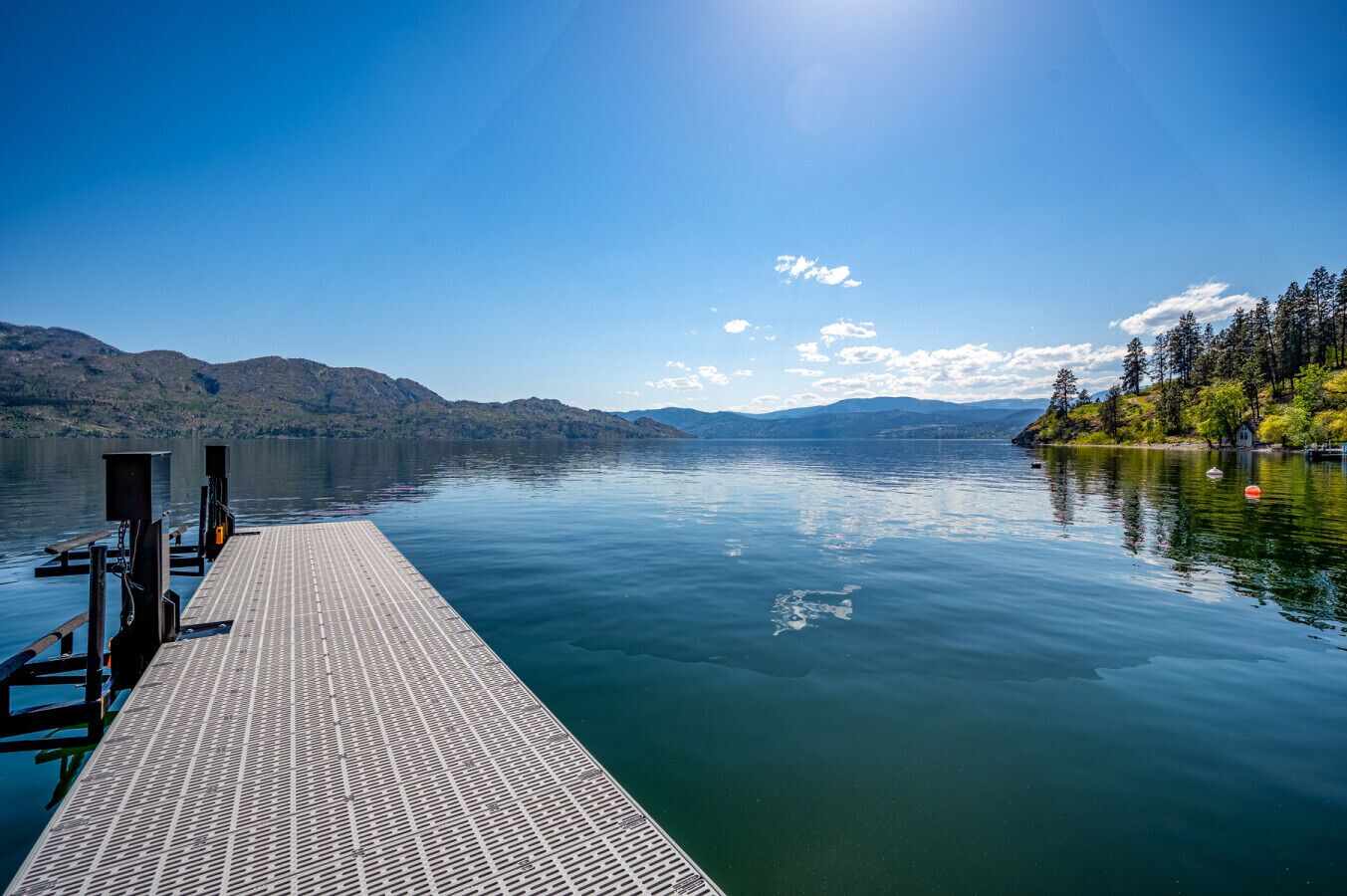 A wooden dock extending into calm lake waters, surrounded by mountains and trees.
