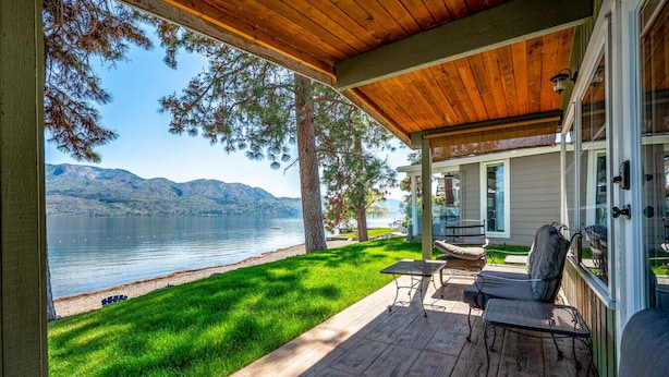 Eine überdachte Terrasse mit Gartenmöbeln mit Blick auf einen See und Berge.