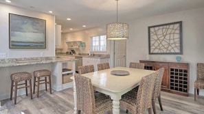 A modern kitchen with a dining area, featuring a large island, wicker chairs, and a pendant light.