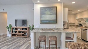A modern kitchen with a marble countertop, two bar stools, a flat-screen TV, and a painting above the counter.