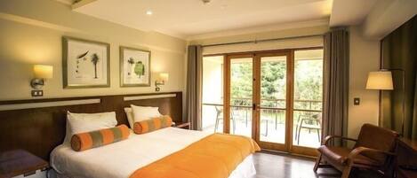 A hotel room with a large bed, a wooden headboard, a balcony with chairs, and framed pictures on the wall.