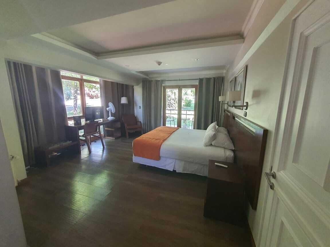 Habitación de hotel con cama, escritorio y silla. Tiene un balcón con vistas a la vegetación.