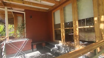 A wooden structure with a red wall, large windows, and a covered outdoor area with steps leading to a seating area.