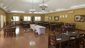 Un comedor amplio con varias mesas y sillas, ventanas grandes y candelabros.