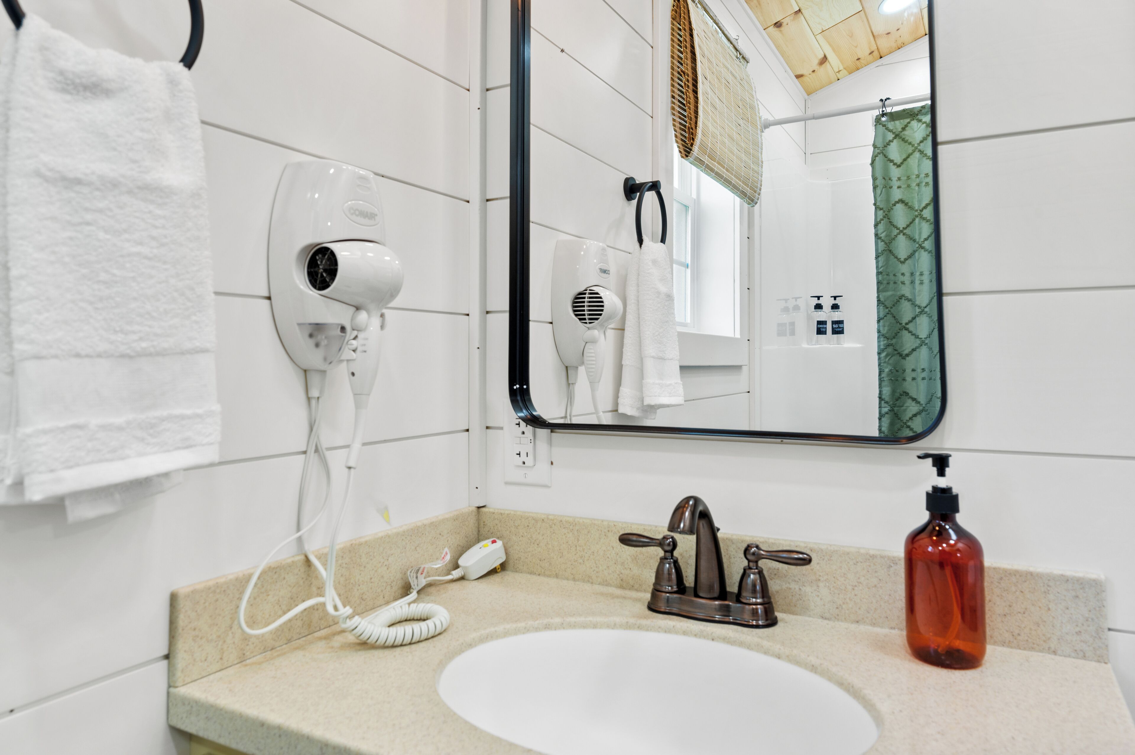 Een badkamer met een witte wastafel, een spiegel, een haardroger en een handdoekhouder.