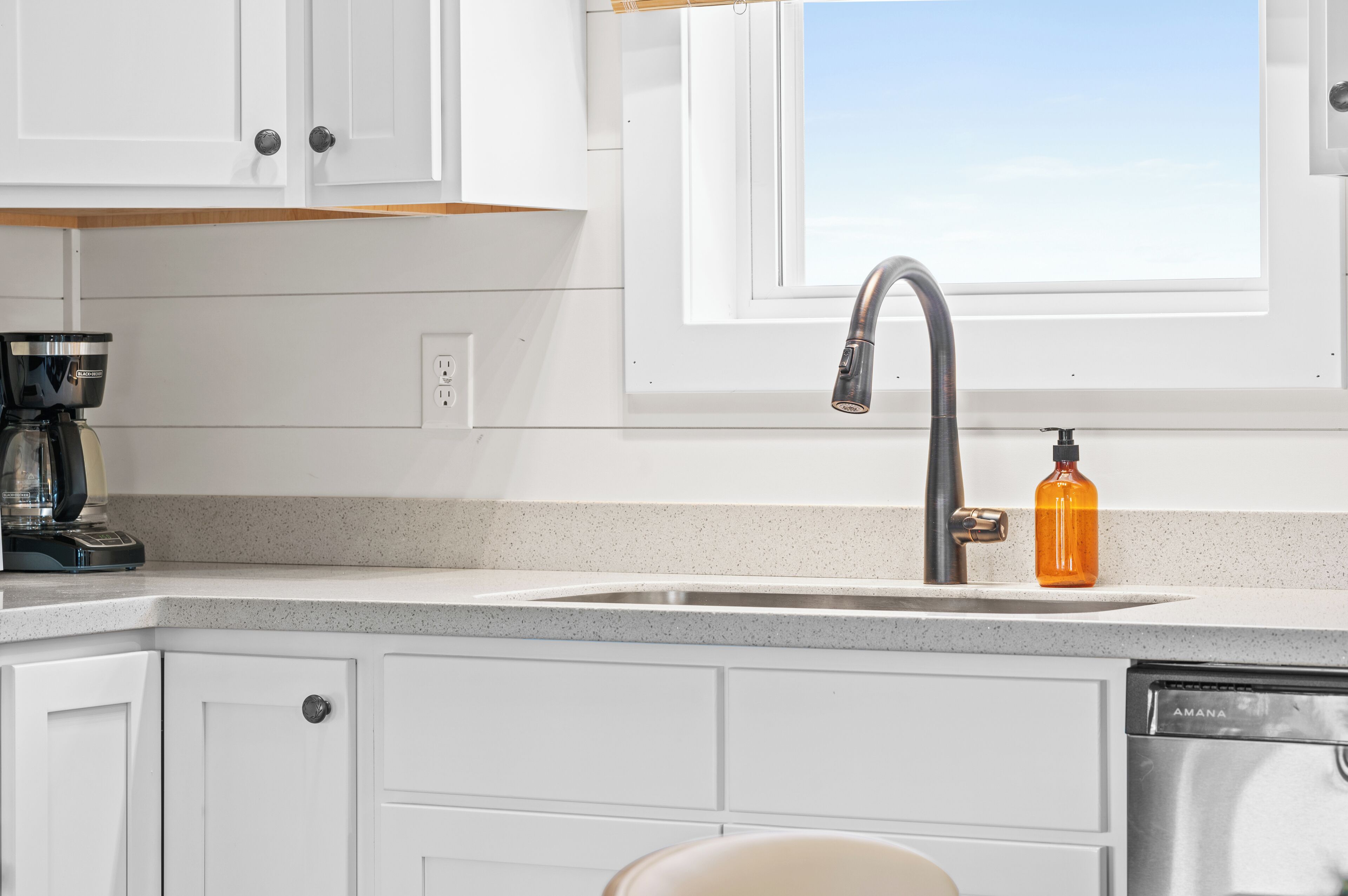 A kitchen with white cabinets, a stainless steel sink, a window above the sink, and a coffee maker on the counter.