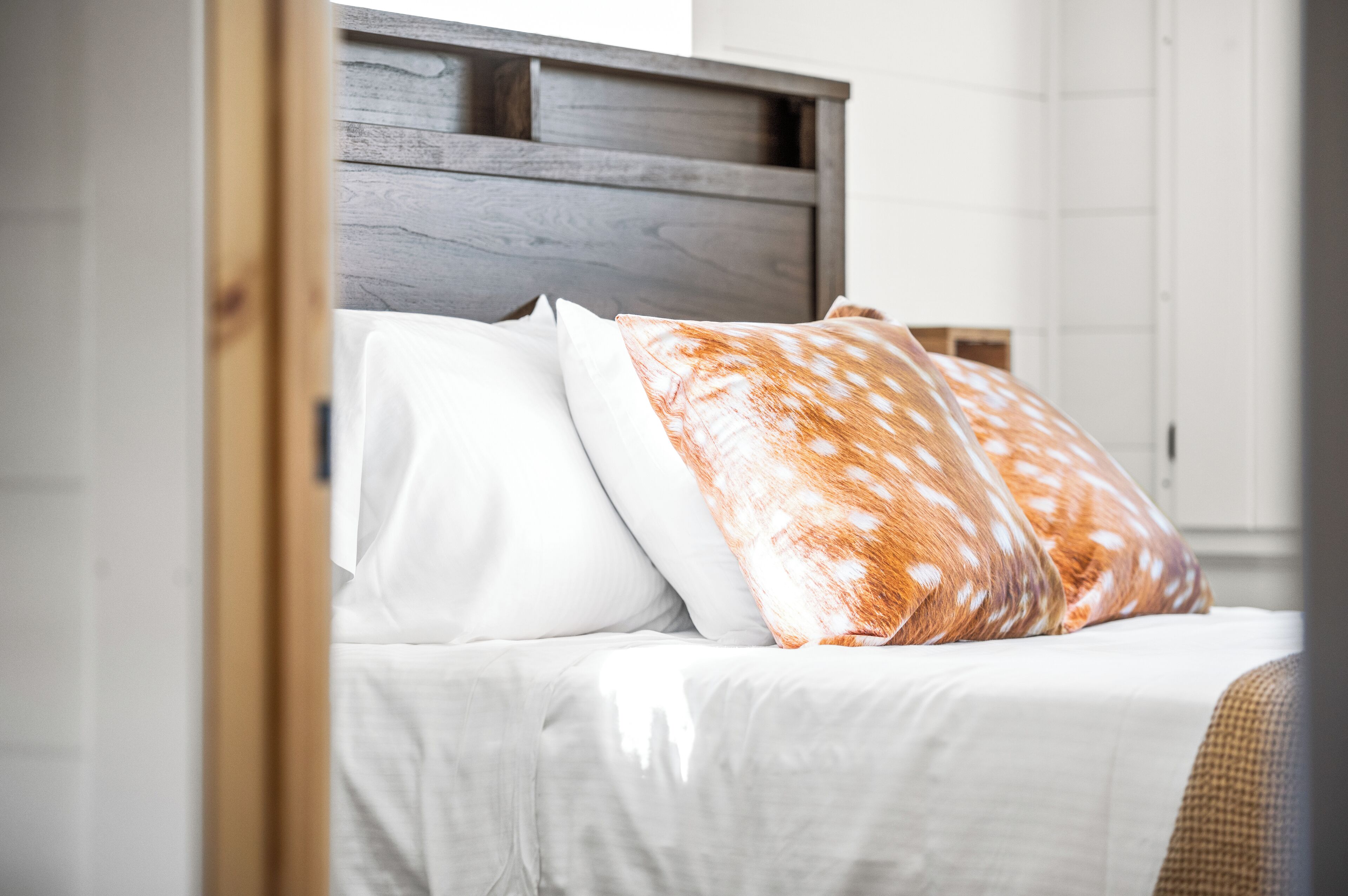 Ein Bett mit hölzernem Kopfteil, weißer Bettwäsche und gemusterten Kissen.