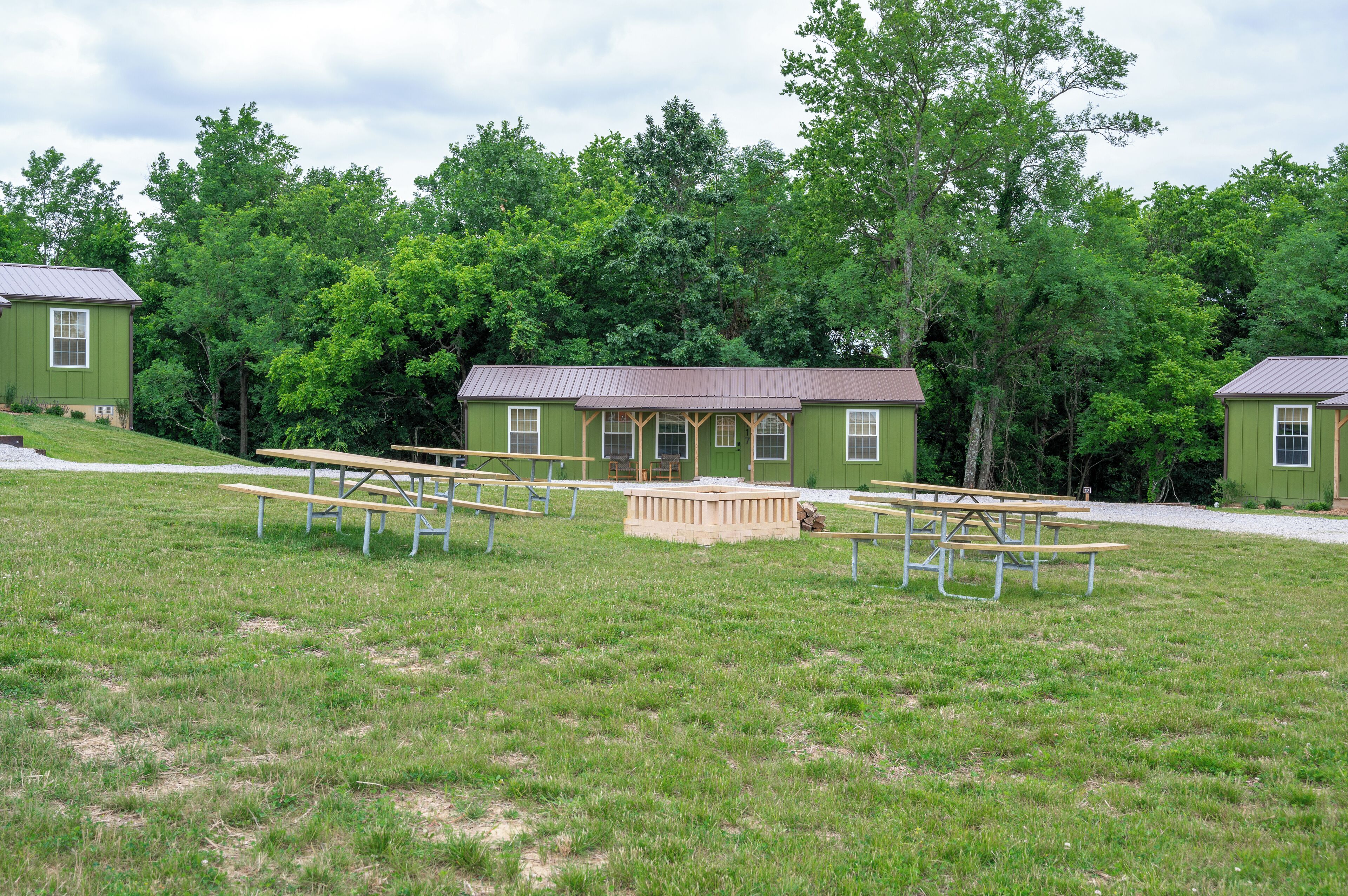 A green building with a porch and picnic tables in a grassy area.
