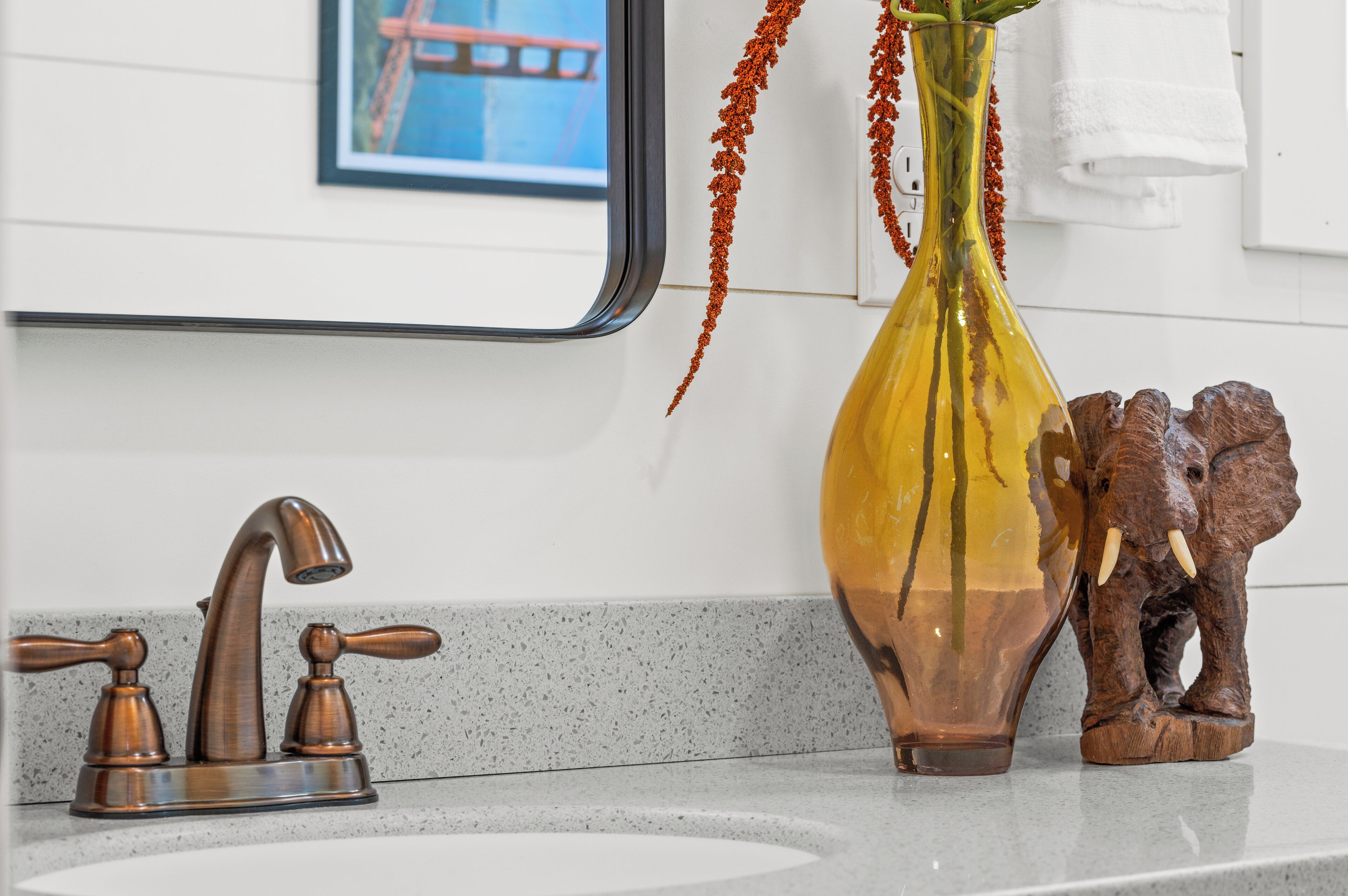 A bathroom sink with a modern faucet, a vase with red flowers, and a wooden elephant figurine.