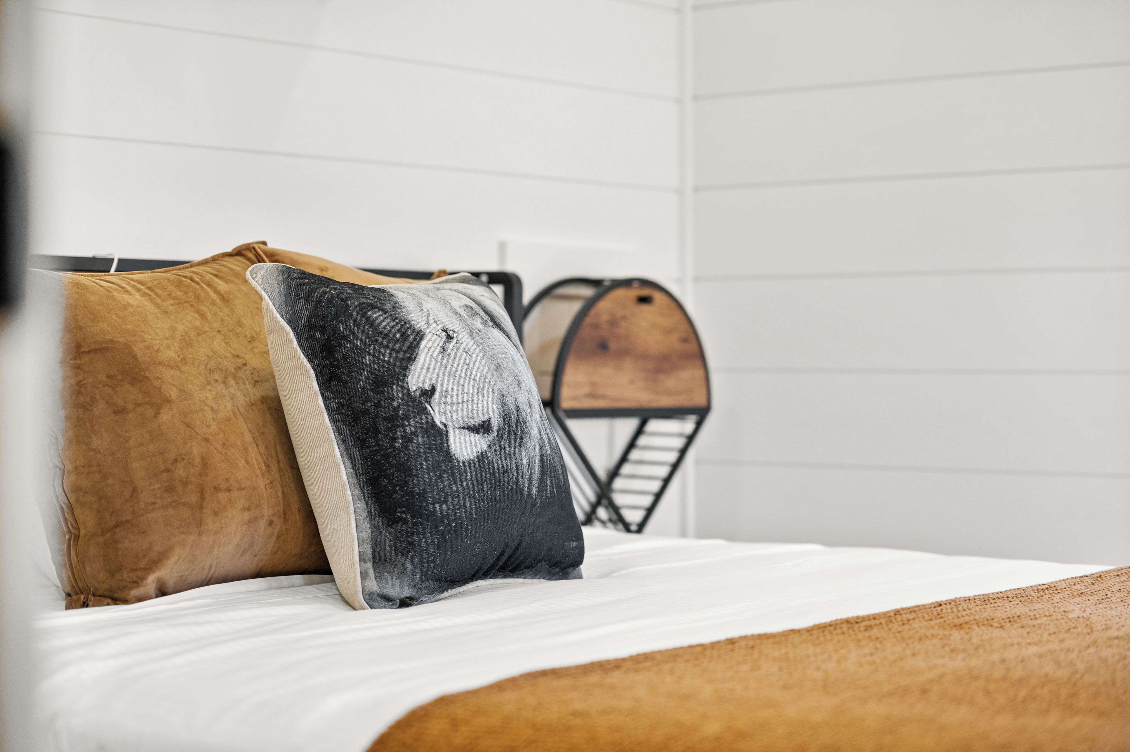 Un letto con due cuscini, uno con il motivo del volto di un leone, e una botte di legno sullo sfondo.