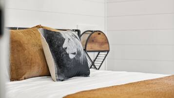 Un letto con due cuscini, uno con il motivo del volto di un leone, e una botte di legno sullo sfondo.