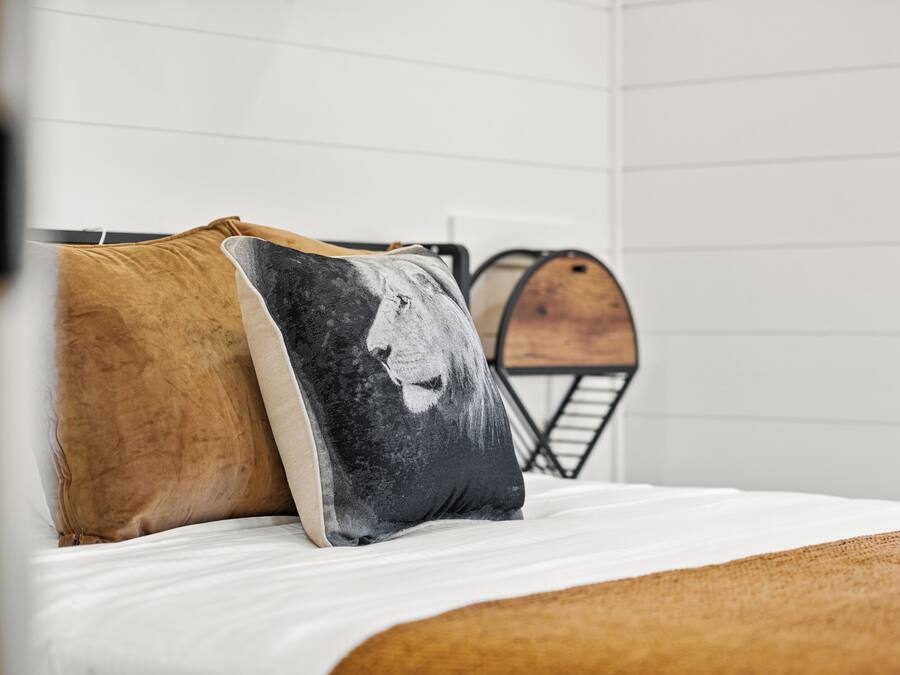 Un letto con due cuscini, uno con il motivo del volto di un leone, e una botte di legno sullo sfondo.