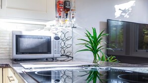 A kitchen with a microwave, a glass-top stove, and a plant. - Cosy 1-bedroom Apartment - Putney High Street (London)