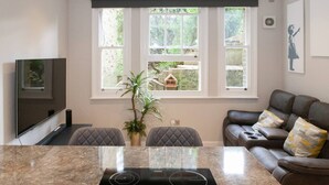 A modern kitchen with a built-in stove, a dining table, and a seating area with a sofa and chairs. - Cosy 1-bedroom Apartment - Putney High Street (London)