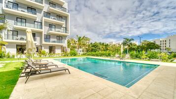 Un hotel moderno con piscina, tumbonas y un jardín bien cuidado.