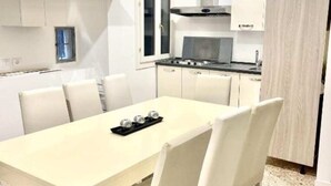 Et moderne køkken med hvide skabe, en sort bordplade og et spisebord med hvide stole.